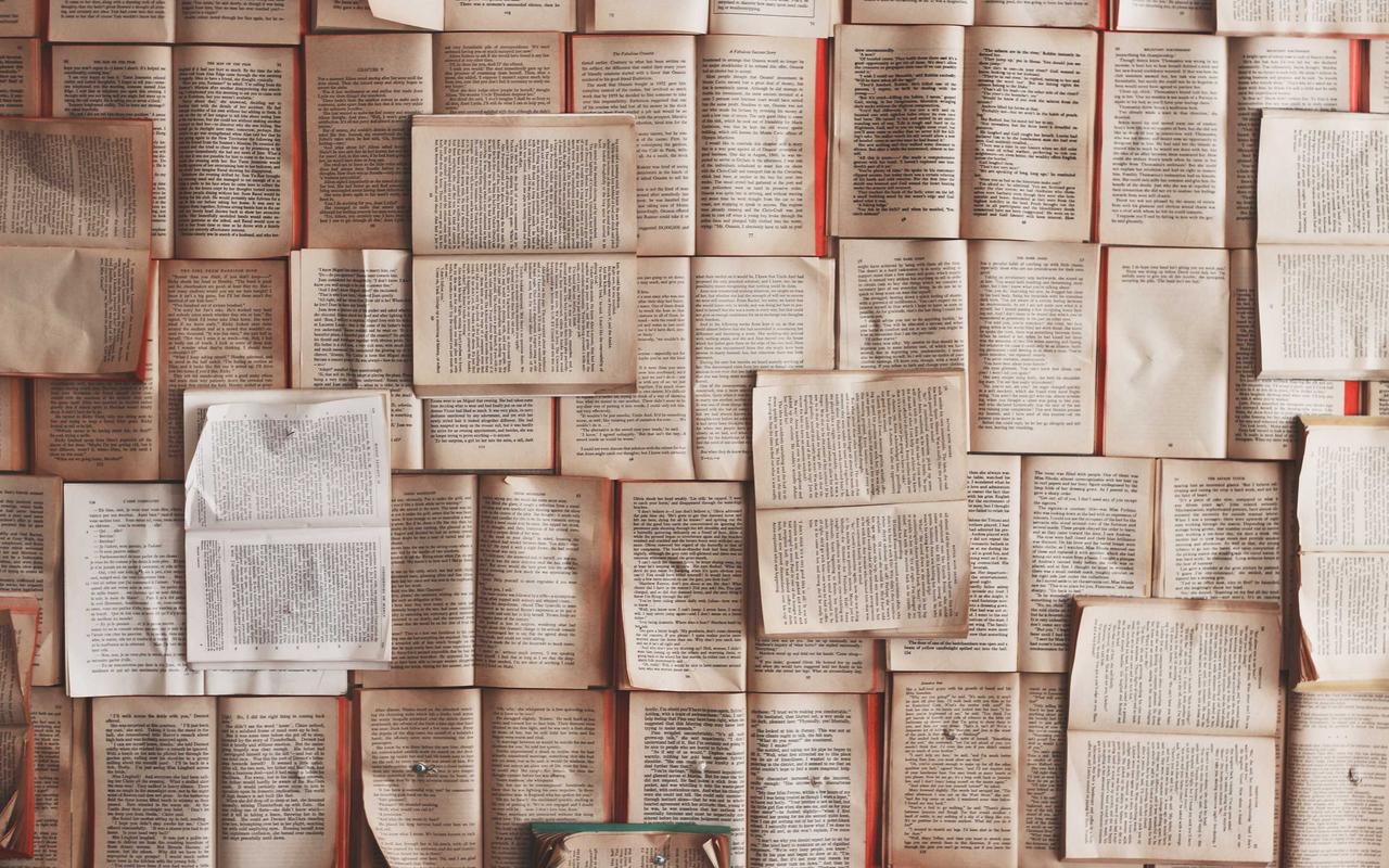 Dozens of open paperback books laid face down side by side, filling the frame with printed pages