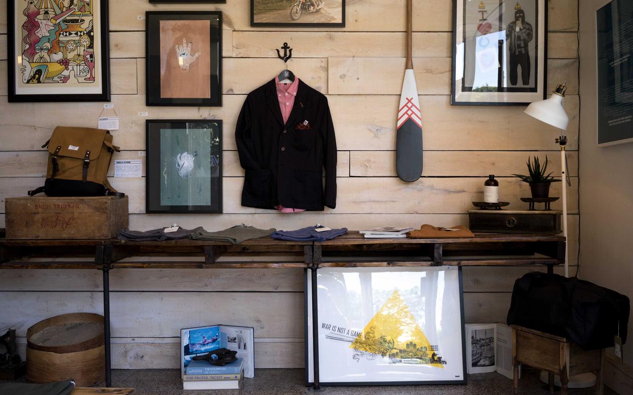 A shop interior in pale wood: a jacket on a hanger between framed prints, with boxes and tools on the shelves below