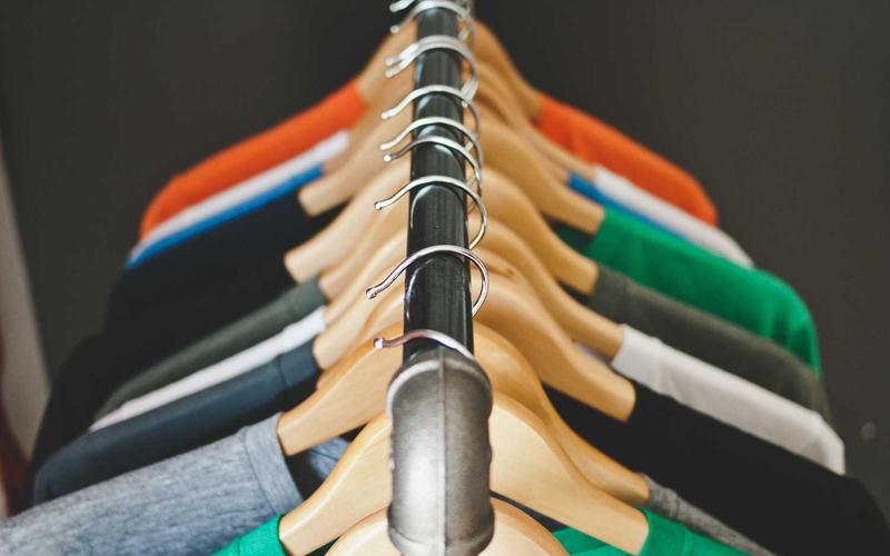 A rail of folded shirts on wooden hangers in orange, green, navy and grey