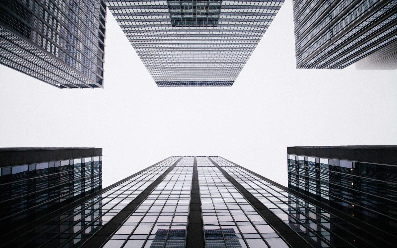 Looking straight up the gap between four glass office towers into a blank white sky